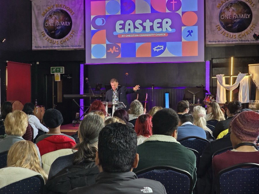 A pastor preaching, viewed from the back of a full and multicultural congregation